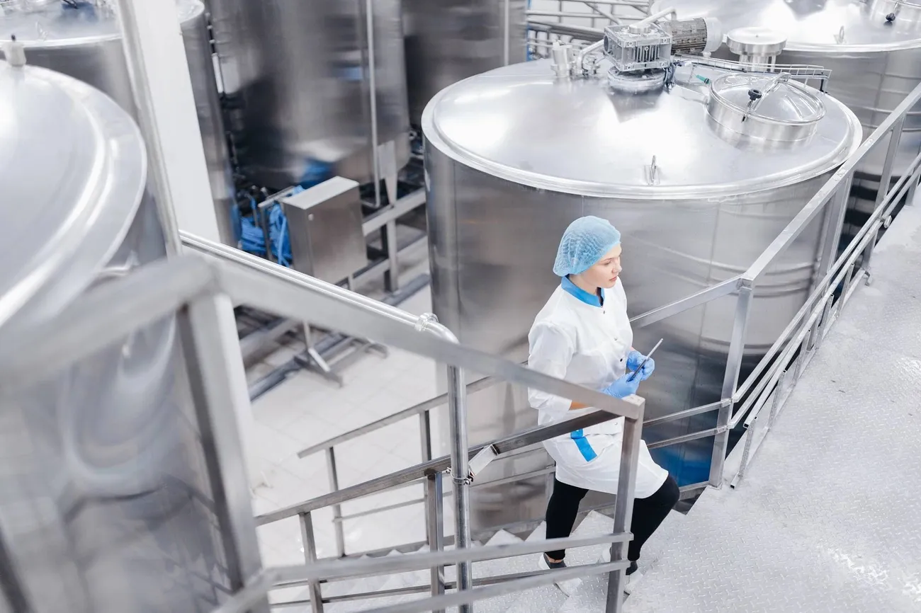 Allergen Cleaning Validation & Verification: Evidence-Based Protocols for UK Food Safety Audits 3 Worker in protective clothing inspecting stainless steel tanks inside a food processing facility.
