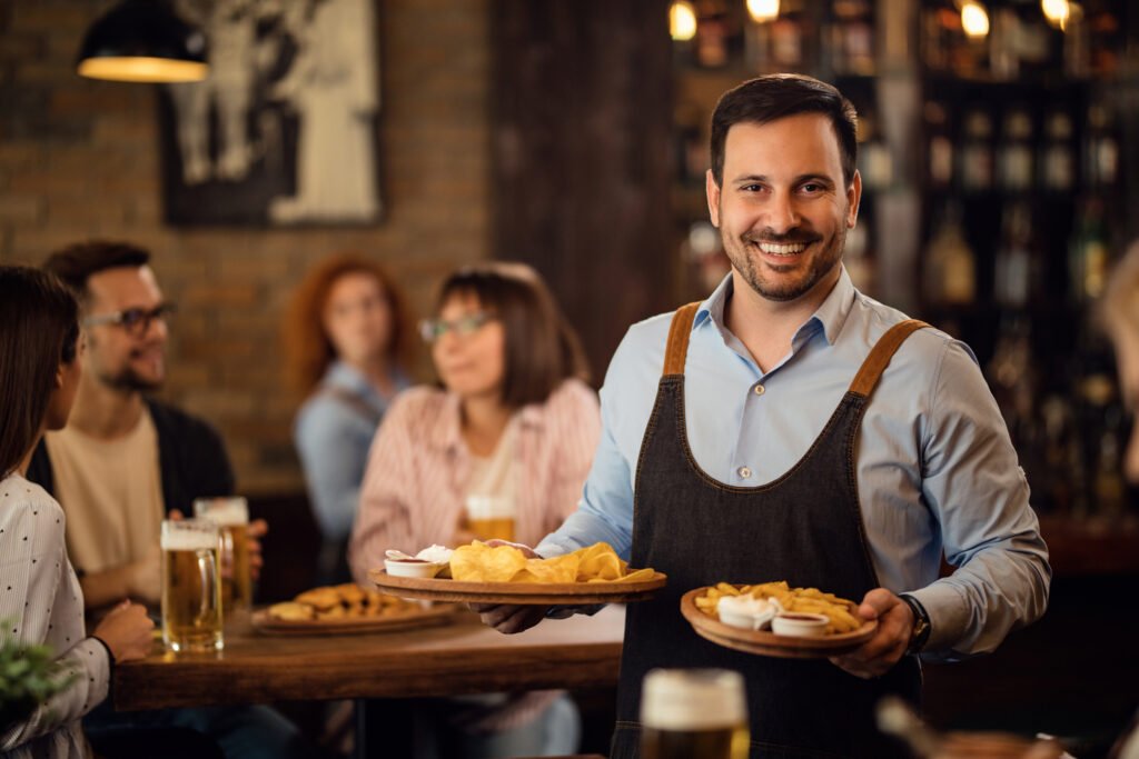 Home 9 happy waiter holding plates with food looking camera while serving guests restaurant 1