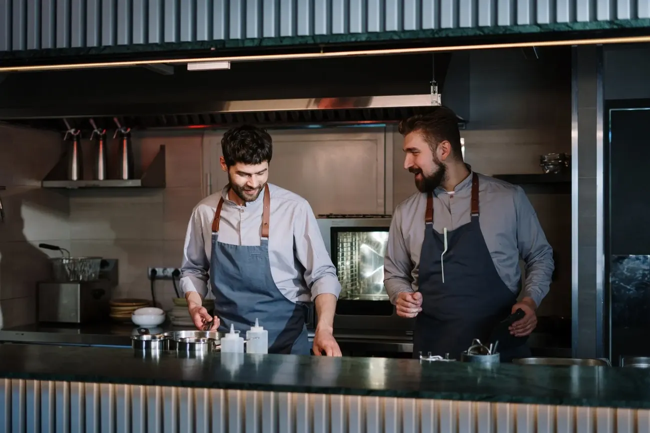 Two chefs in aprons working together in a professional kitchen focused on allergen management training.