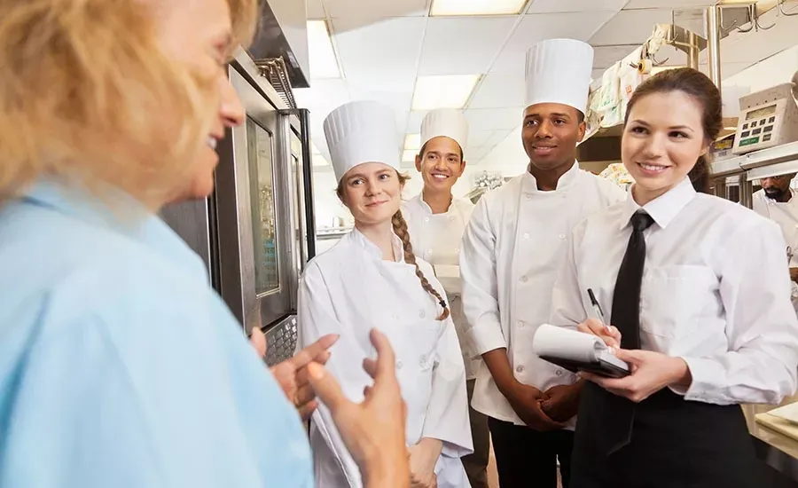 Food safety trainer instructs a group of chefs and staff in a professional kitchen setting.