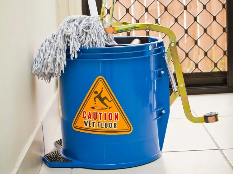 Blue mop bucket with caution wet floor sign and mop head, used for cleaning to prevent allergen cross contamination.