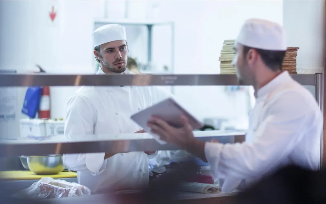 Two chefs in a kitchen discussing food safety, highlighting cross contamination in halal certification.