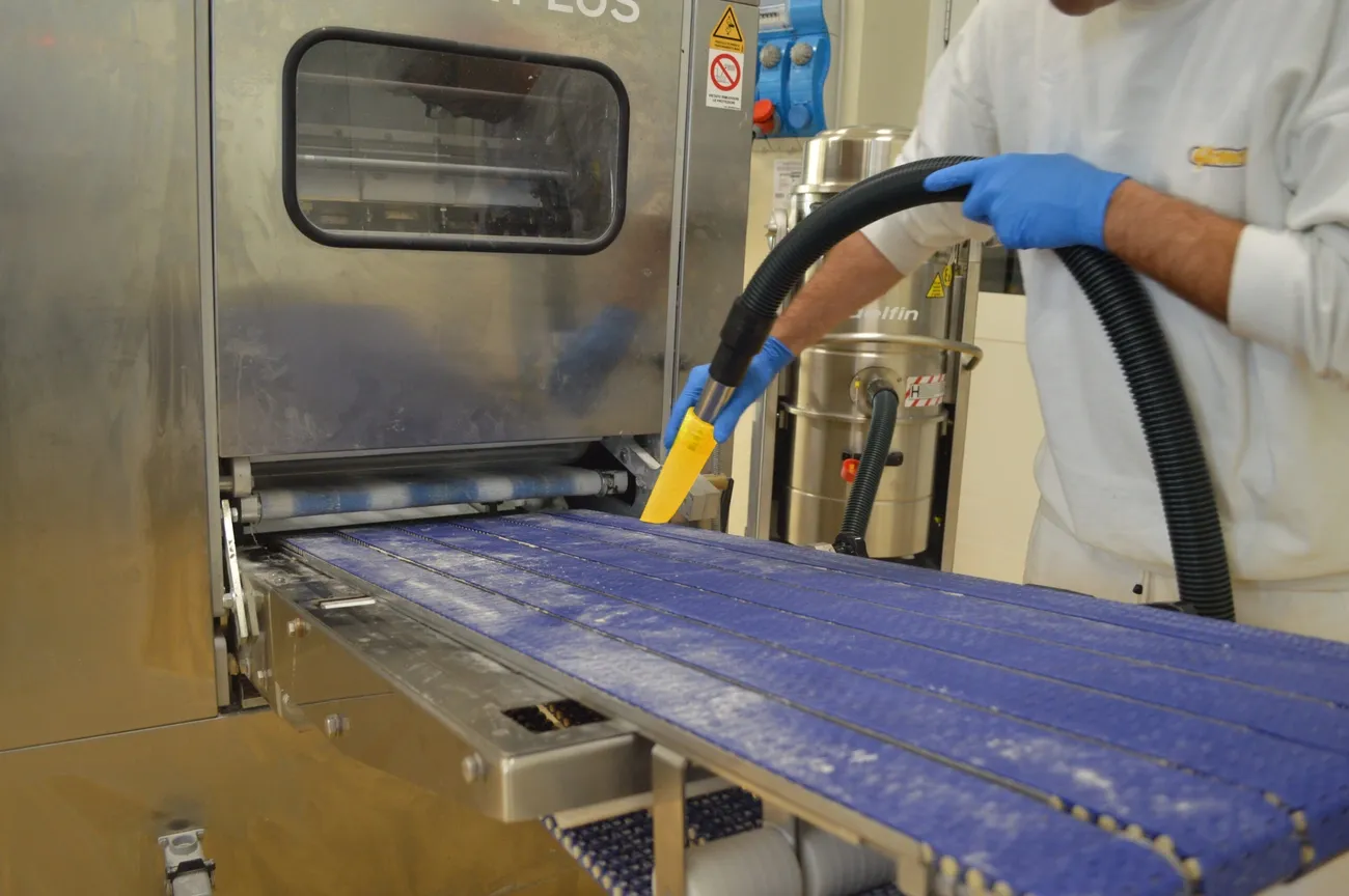 Worker wearing gloves cleans a conveyor belt in a food processing plant to prevent cross contamination.