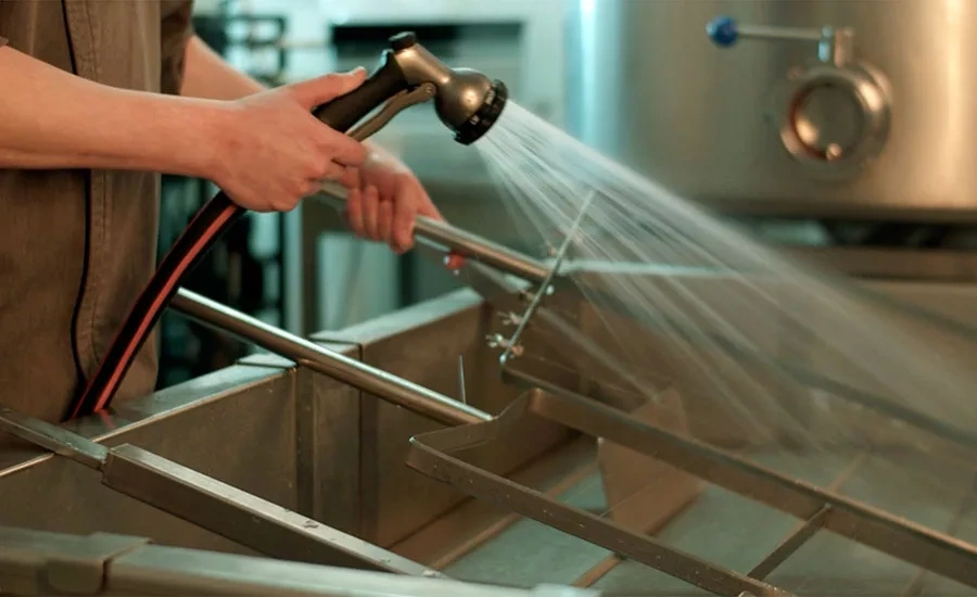 Person using a spray hose to clean stainless steel equipment in a food safety environment for allergen control.