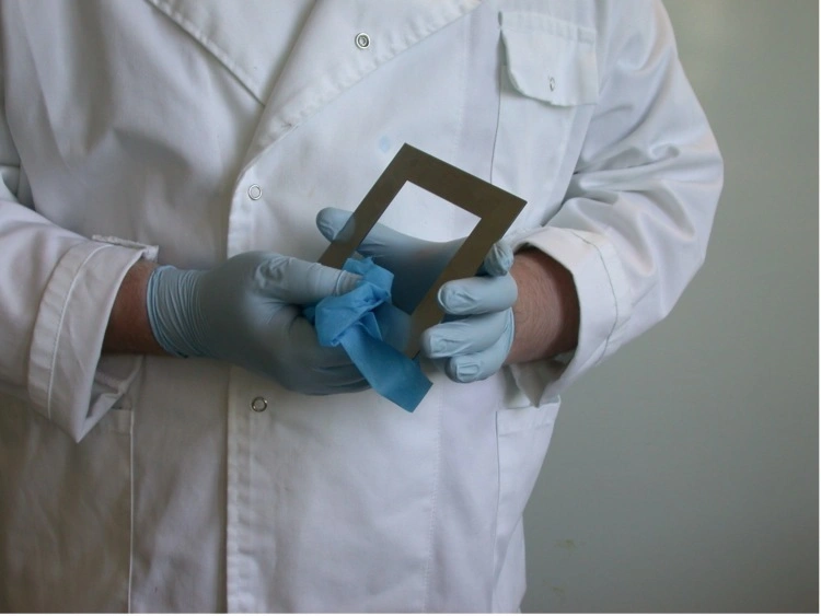 Person in a white lab coat and gloves cleaning a metal frame, representing microbial monitoring.